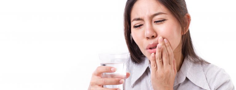 Mulher segurando copo de água | O que causa sensibilidade nos dentes?