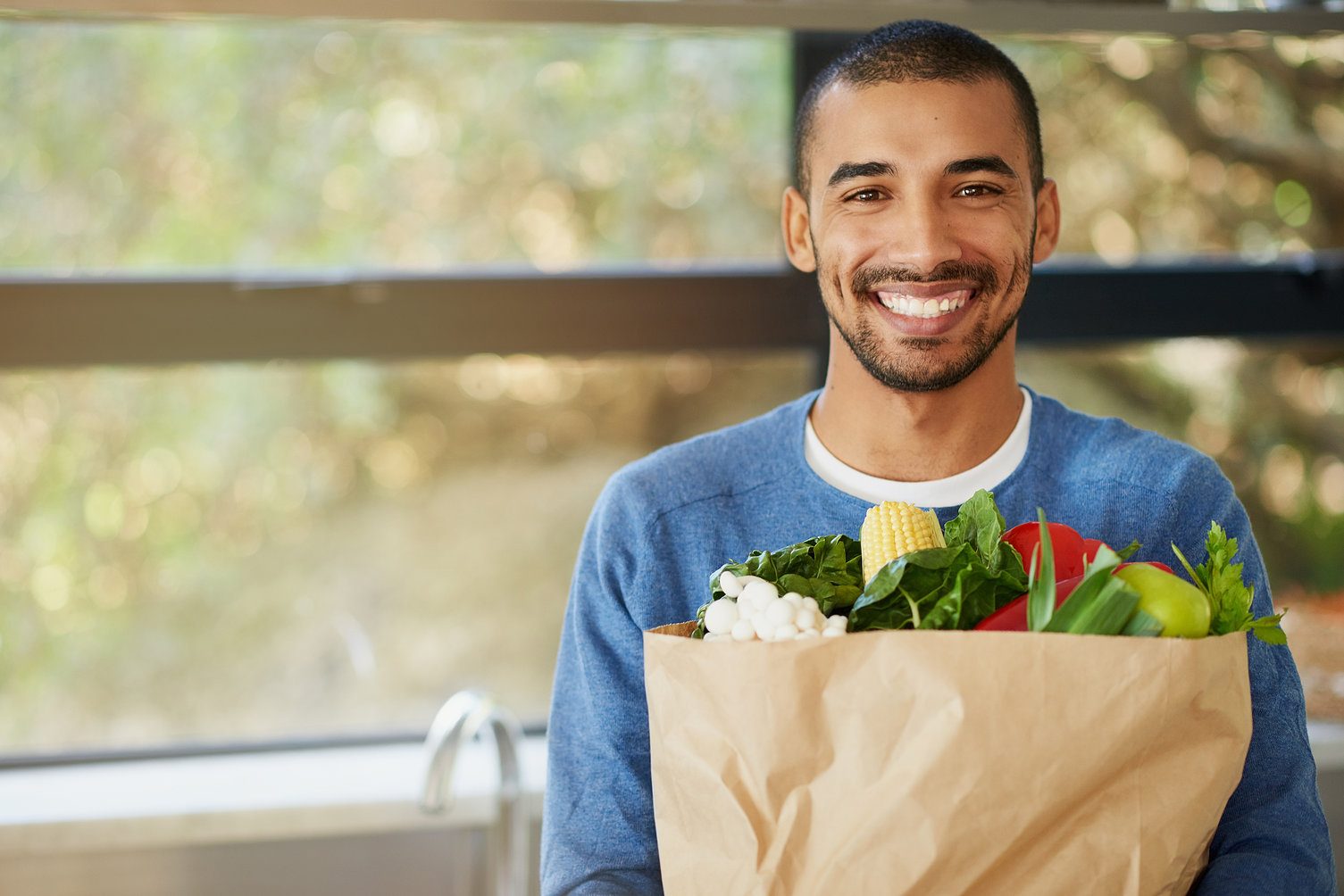 homem negro sorrindo segurando sacola de papel com frutas e legumes dentro | Como a alimentação pode influenciar na saúde bucal?