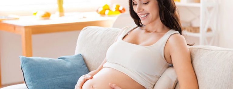 Mulher grávida sentada com as mãos na barriga e olhando para ela | Cuidados com a saúde bucal durante a gravidez